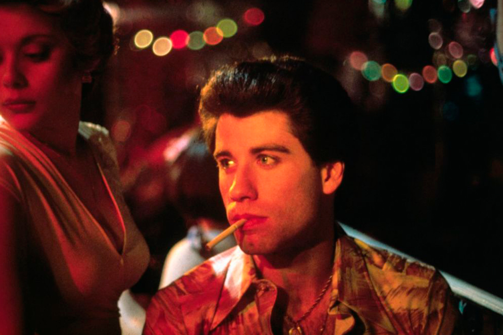 Cena de 'Embalos de Sábado a Noite', em que o ator John Travolta aparece com um cigarro na boca sentado ao lado de uma mulher.