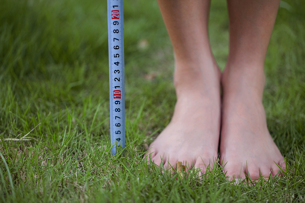 Close up de pés de uma pessoa, na grama, com uma fita métrica ao lado.