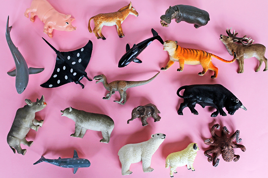 Diversos brinquedos de animais de espécies variadas, dispostos sobre fundo cor de rosa.