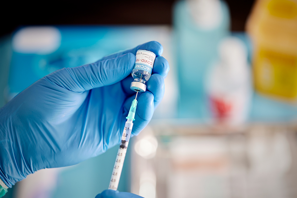 Close up das mãos de uma pessoa manuseando uma seringa e um frasco de vacina contra Covid-19.