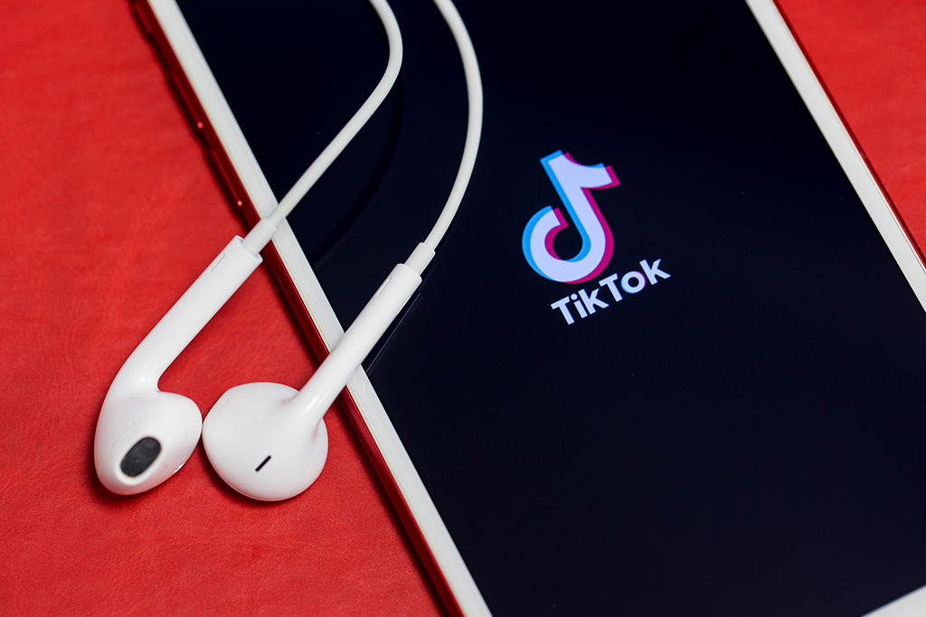 Close de um celular exibindo a logo do TikTok na tela. Ao lado, fones de ouvido.