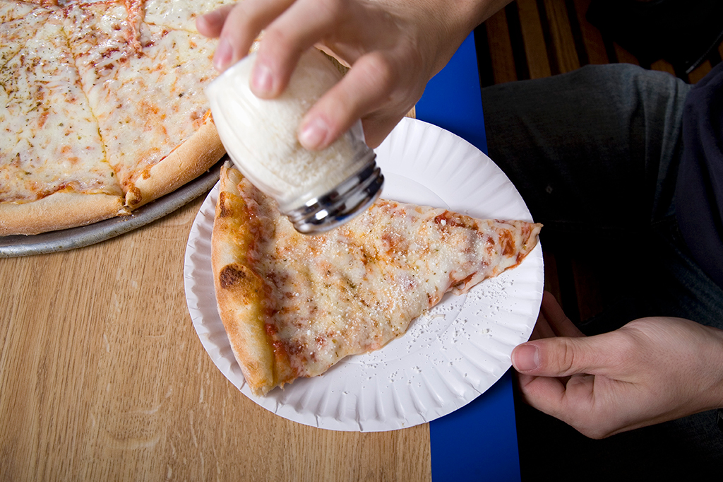 Pessoa adicionando sal à uma fatia de pizza.
