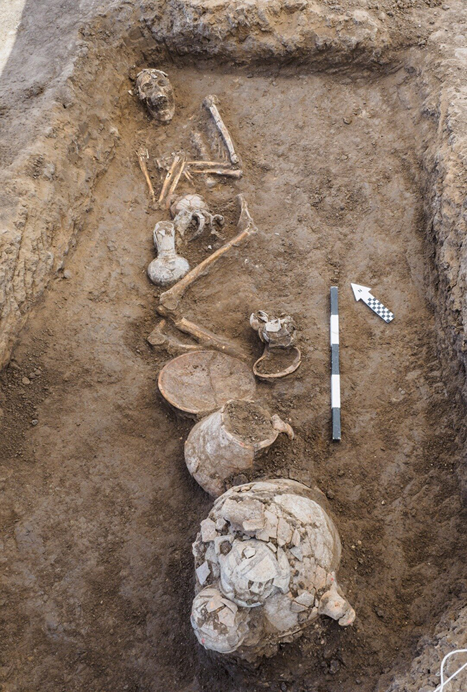 Escavação mostrando esqueleto e cerâmicas encontrados.