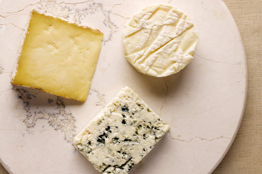 Fotografia de uma tábua de mármore com três tipos de queijo em cima.