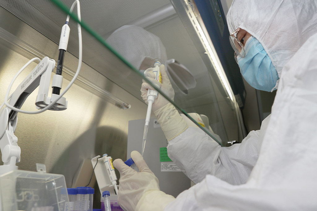 Uma pessoa com EPIs, em laboratório, realizando processo de produção da vacina.