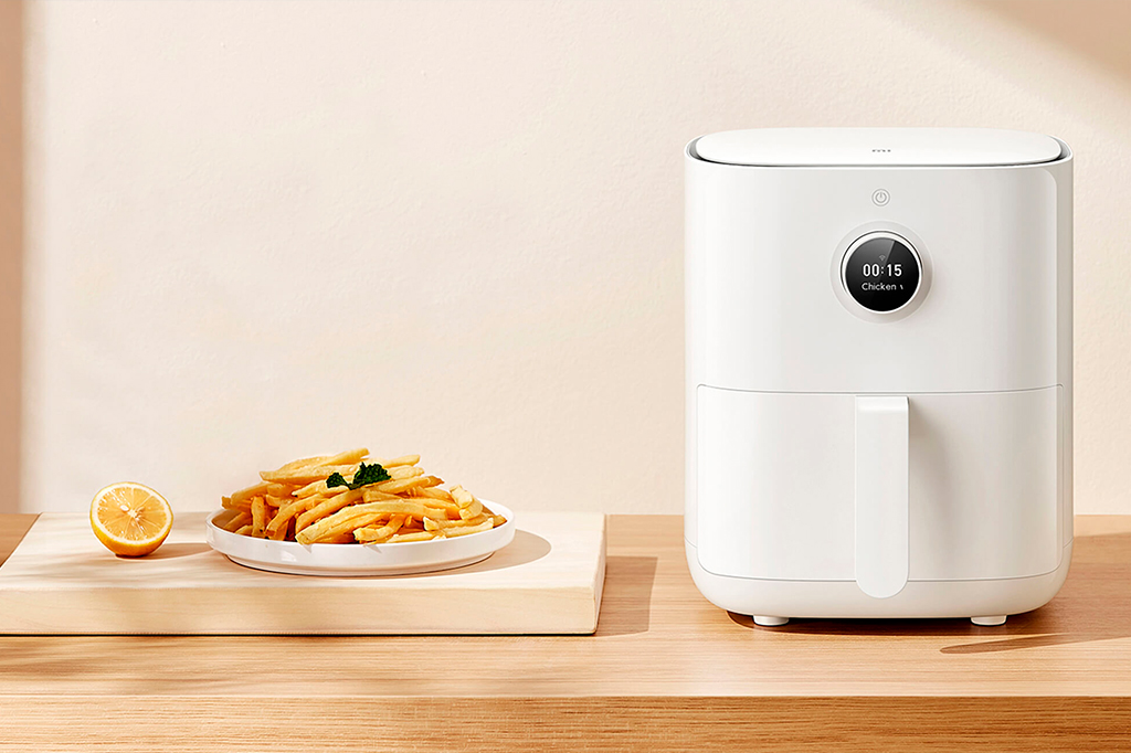 Airfryer Xiaomi em cima de uma bancada de madeira em ambiente iluminado. Ao lado, uma porção de batatas fritas.
