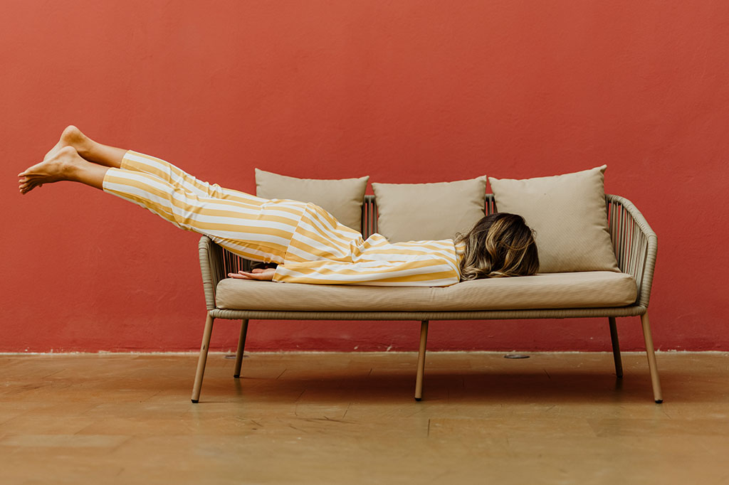 Fotografia de uma mulher dormindo de barriga pra baixo em um sofá.