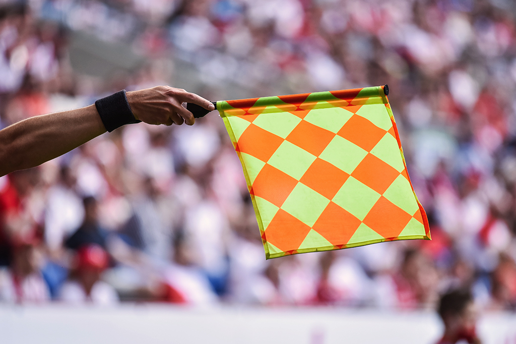 Árbitro levantando a bandeirinha de impedimento numa partida de futebol.
