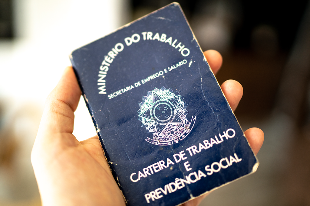 Foto de uma mão segurando uma carteira de trabalho brasileira.