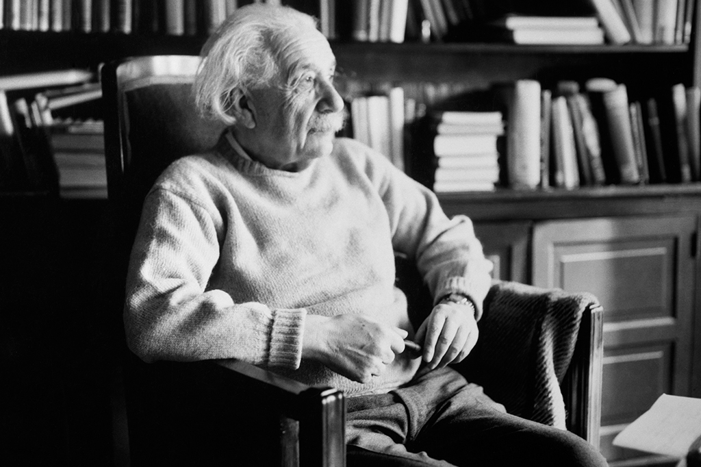 Retrato de Albert Einstein sentado em uma poltrona em uma biblioteca.