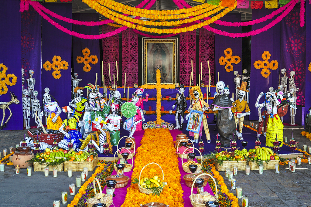 Foto de um altar para o dia dos mortos com oferendas, flores, caveiras e bandeiras.