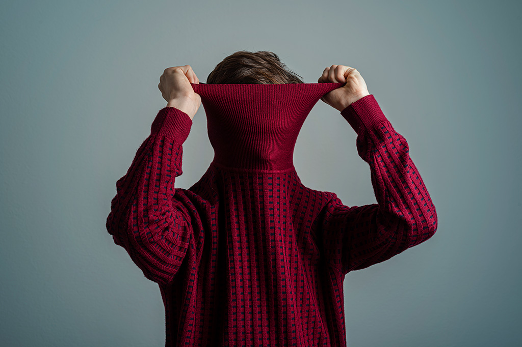 Fotografia de uma pessoa puxando seu suéter por cima da cabeca.