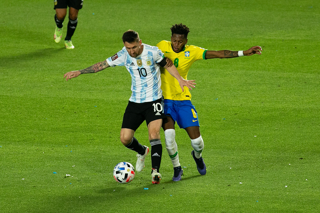 Fotografia de dois jogadores, um do Brasil e outro da Argentina se enfrentando pela posse da bola no campo.