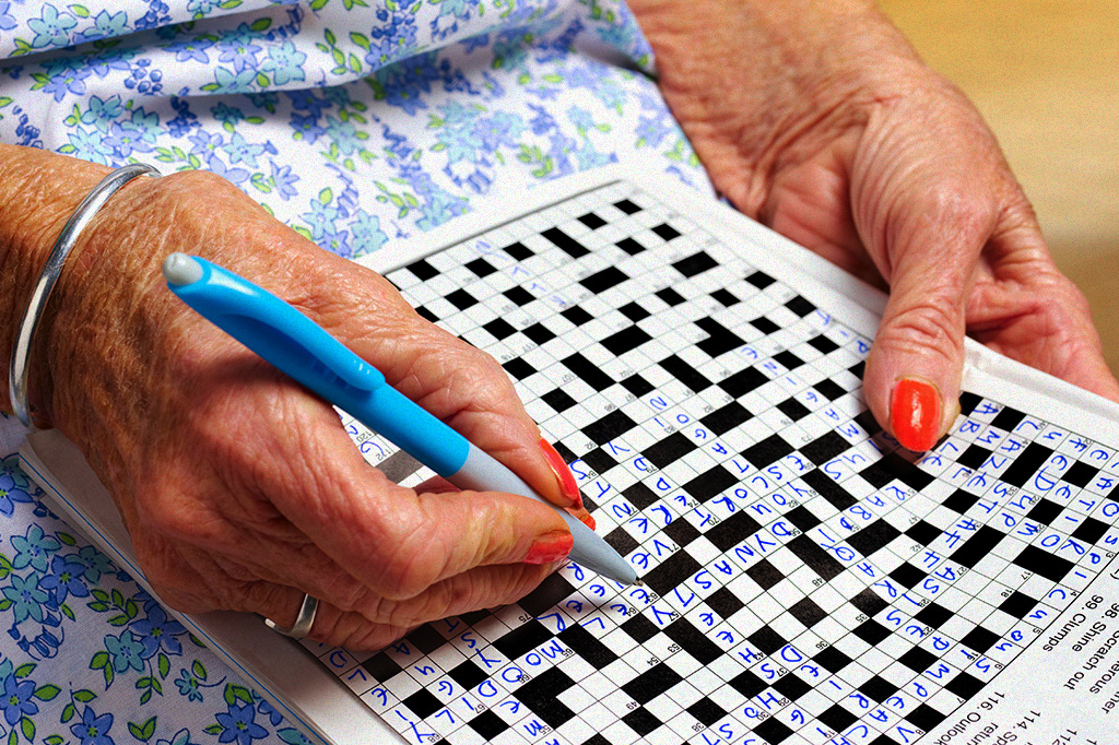Foto mostrando as mãos de uma mulher idosa fazendo palavras-cruzadas.