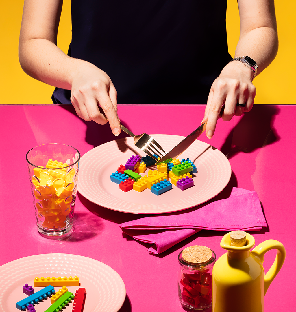 Foto de uma pessoa se servindo em uma mesa onde os alimentos e bebidas são pedaços de lego.