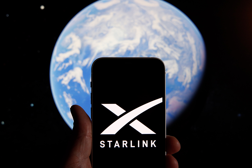 Smartphone exibindo o logo da Starlink no visor, em primeiro plano. Ao fundo, uma imagem desfocada do planeta Terra.