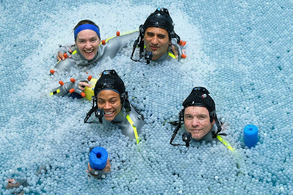 Atores e atrizes do elenco de Avatar nos bastidores, em uma piscina com bolinhas de plástico.
