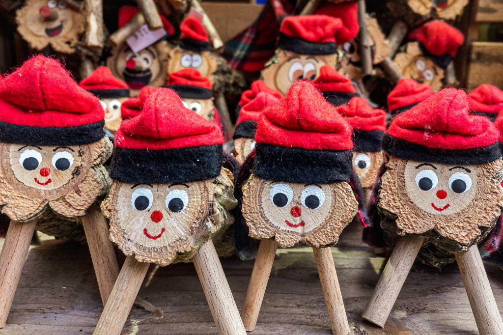Vários Tiós em exposição em um mercado de Natal. Os Tiós estão em pé, sobre duas ou quatro pernas de pau, com um rosto sorridente pintado na ponta, e um gorro vermelho.