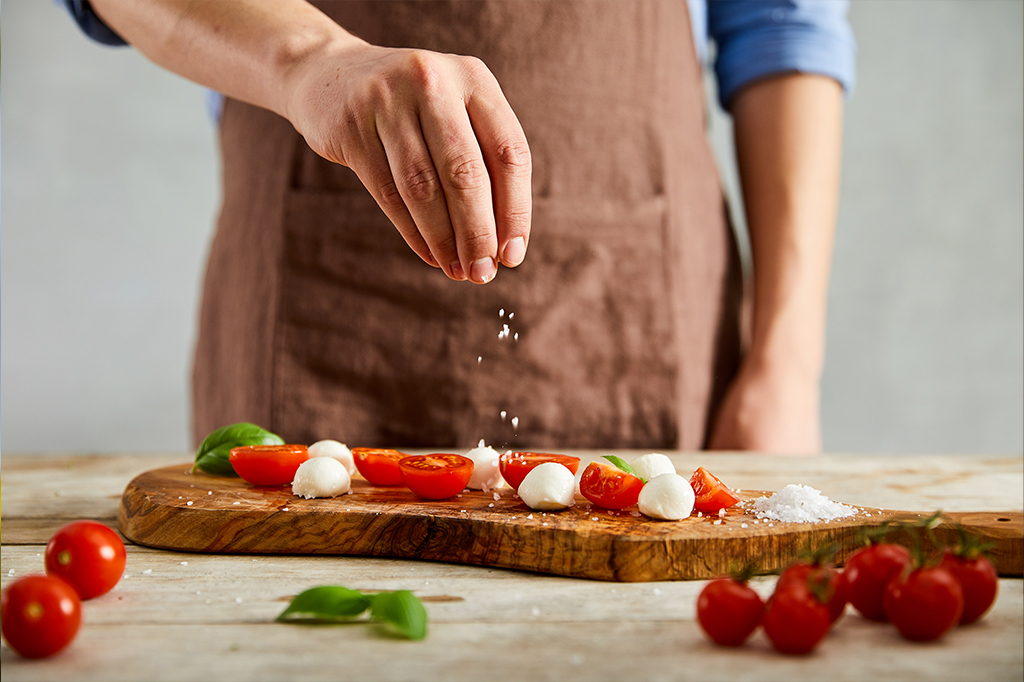 Uma pessoa adicionando sal à tomates cortados em um tábua de madeira.