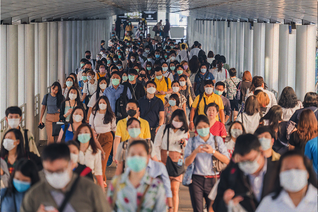 Multidão de pessoas asiáticas indo para o trabalho na hora do rush. A maioria usa máscara.