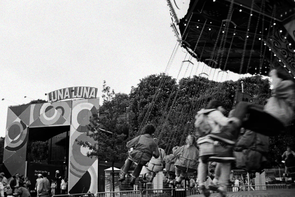 lunaluna_site2 Foto em preto e branco na qual podemos ver o letreiro do parque Luna Luna e algumas crianças brincando no brinquedo