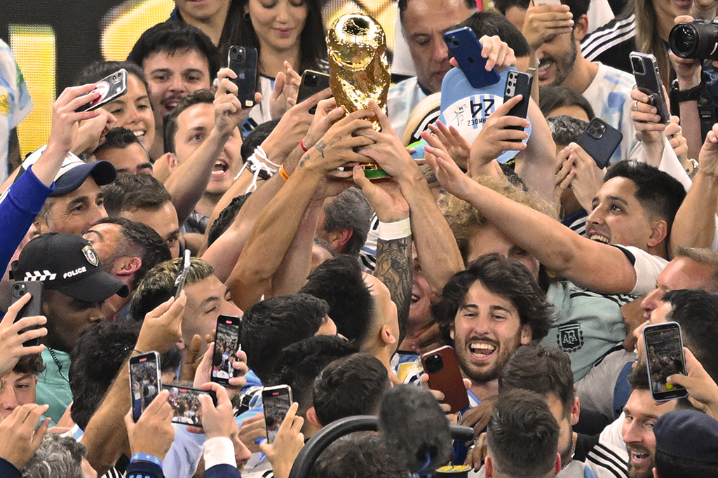 Foto de vários jogadores da Argentina e torcedores tocando na taça da Copa do Mundo.
