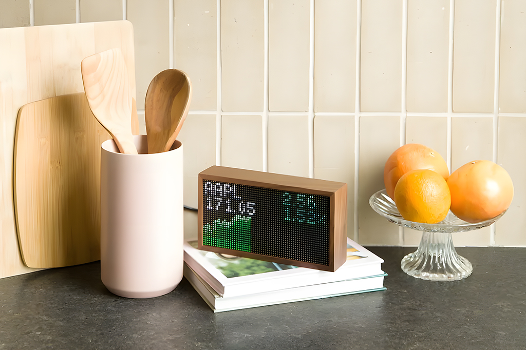 O visor Tidbyt em uma bancada, ao lado de utensílios de cozinha.
