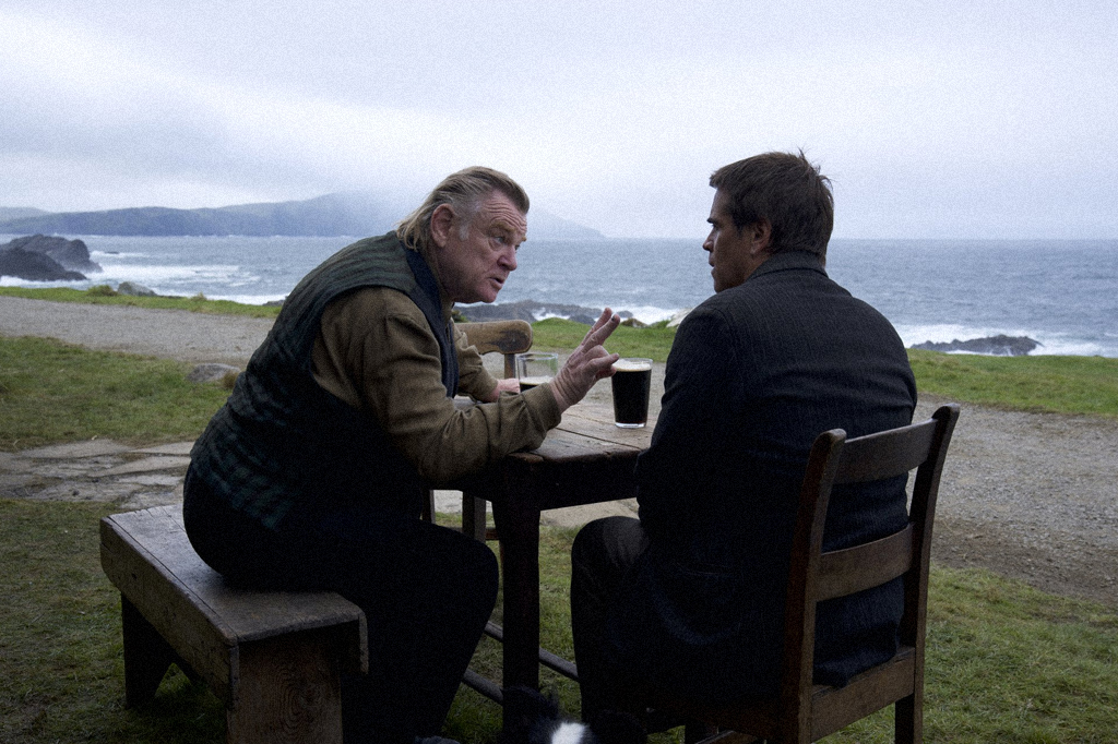 Os personagens principais sentados à mesa, em ambiente aberto com a paisagem da ilha. Parecem estar discutindo.