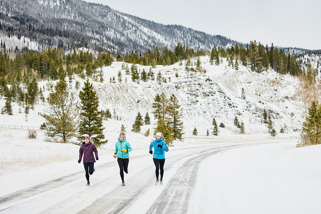 Grupo de três pessoas correndo em uma paisagem coberta por neve.