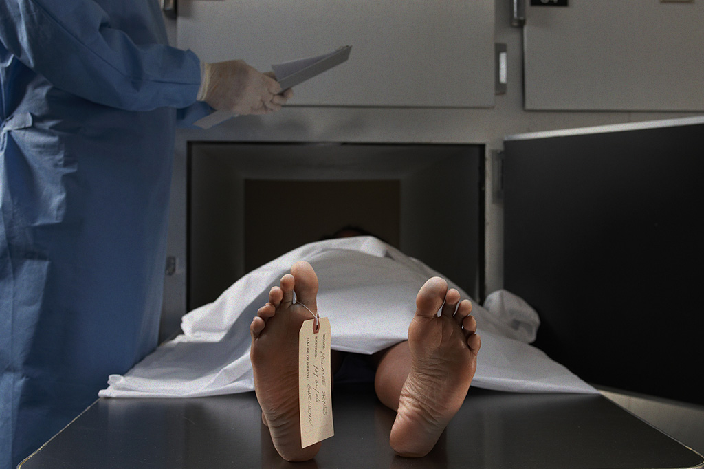 Foto de um especialista analisando um corpo coberto, em um necrotério.