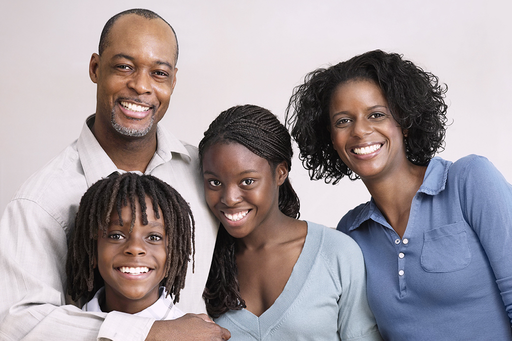 Foto de uma família negra composta por um pai, uma mãe e dois filhos sorrindo para a câmera.