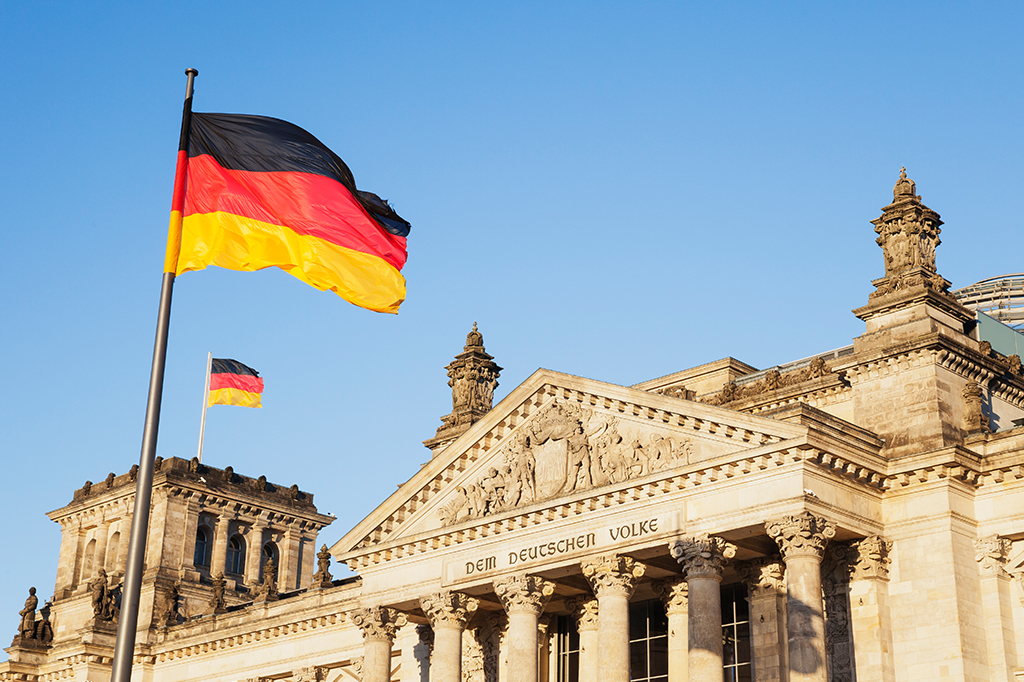 Fotografia do Parlamento Federal da Alemanha, com a fachada escrito "Dem Deutschen Volke" e bandeiras do país.
