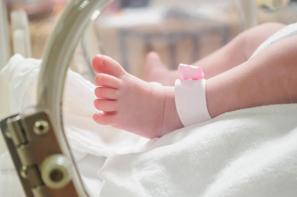Close no pé de um bebezinho recém nascido com uma tornozeleira de identificação.