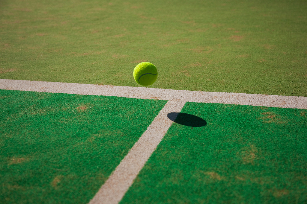 Close de uma bola de tênis prestes a tocar o chão da quadra.