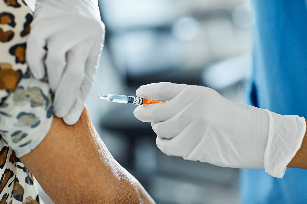 Foto-detalhe de uma pessoa sendo vacinada por trabalhador de saúde, no braço.