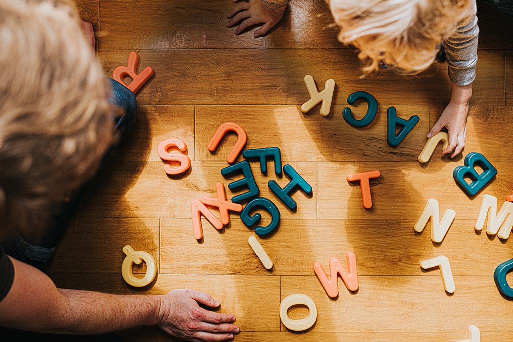 Fotografia de uma criança e um adulto brincando com letras.