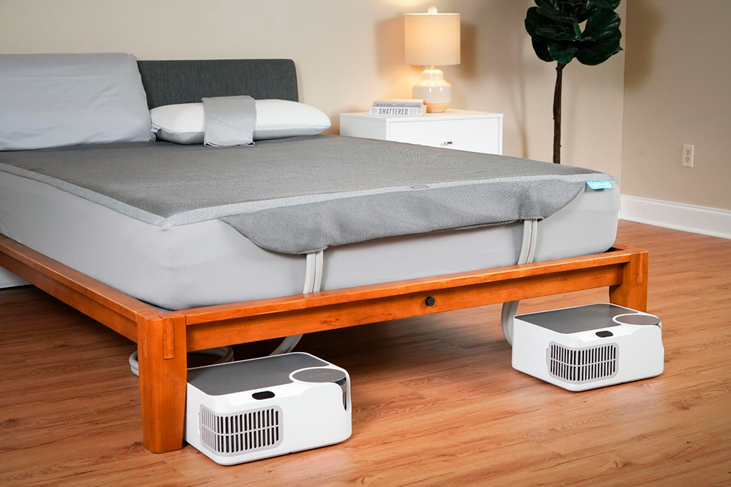 Foto de aplicação do produto Sleepme Dock Pro, onde uma manta esticada sob a cama é conectado a dois compressores alocados no chão.