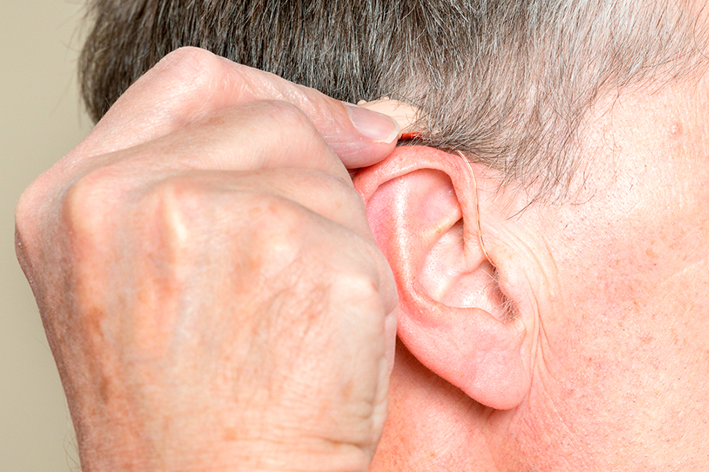 Foto aproximada de um aparelho auditivo moderno pequeno atrás da orelha de um homem idoso.