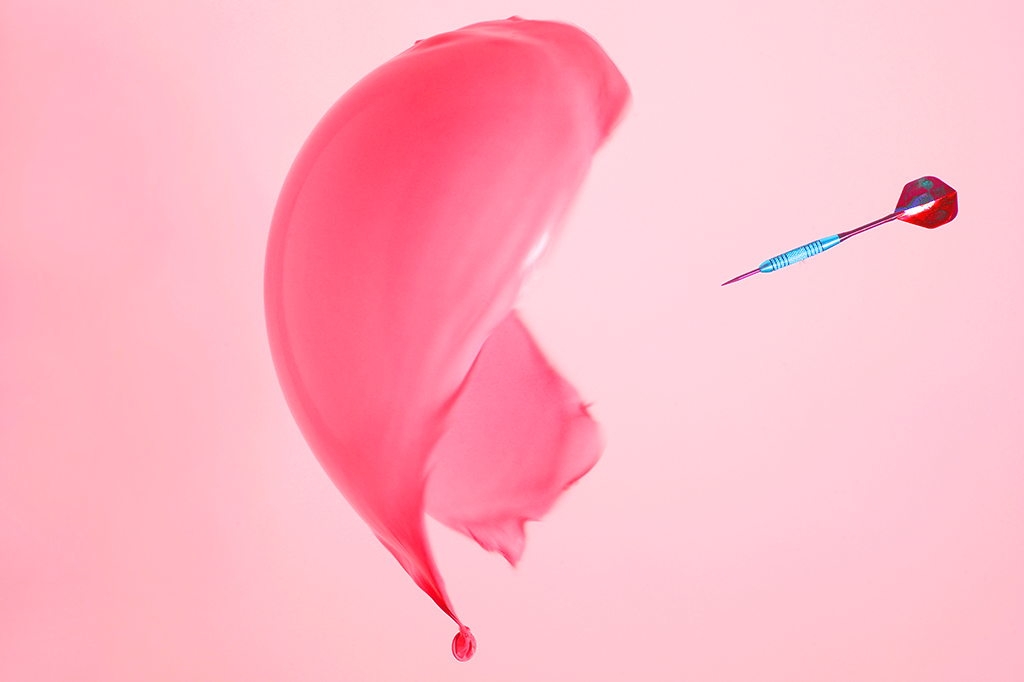 Fotografia de um balão sendo estourado por um dardo.