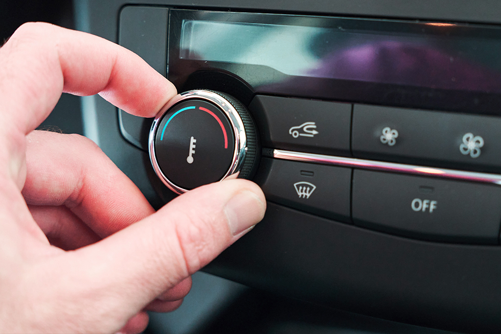 Close de uma mão ajustando a temperatura do ar condicionado de um carro.