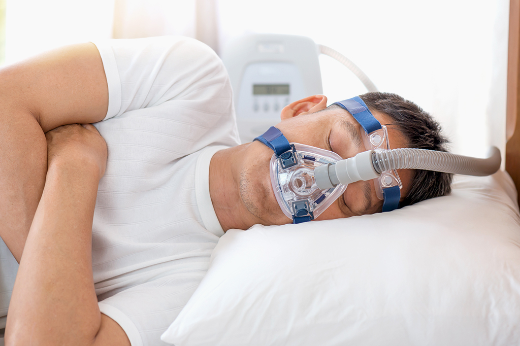 Homem dormindo na cama usando a máscara CPAP para o tratamento de apneia do sono.