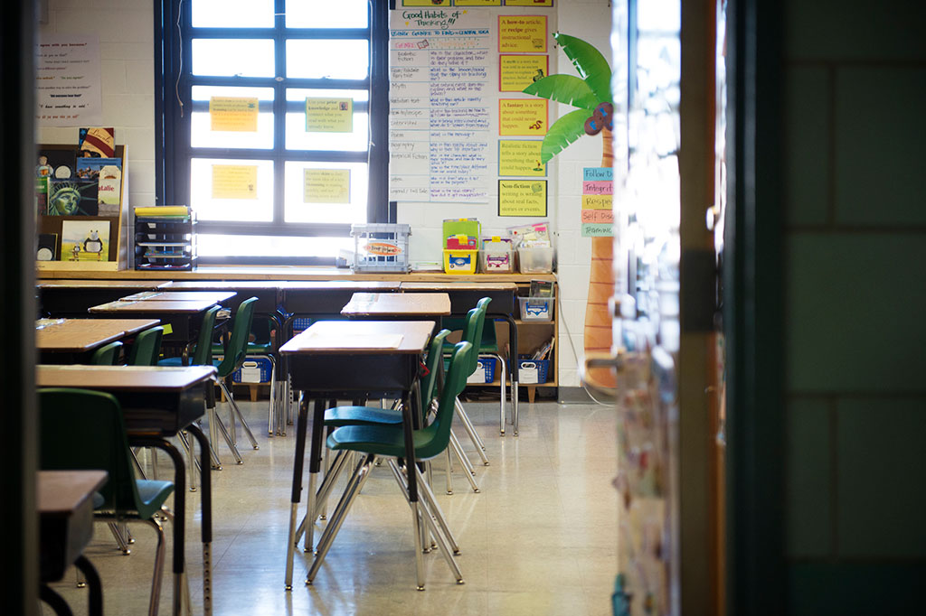 Foto do interior de uma sala de aula vista através da fresta da porta.