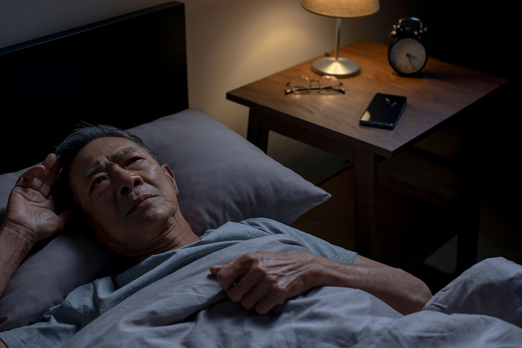 Foto de homem asiático idoso deitado na cama sem conseguir dormir.