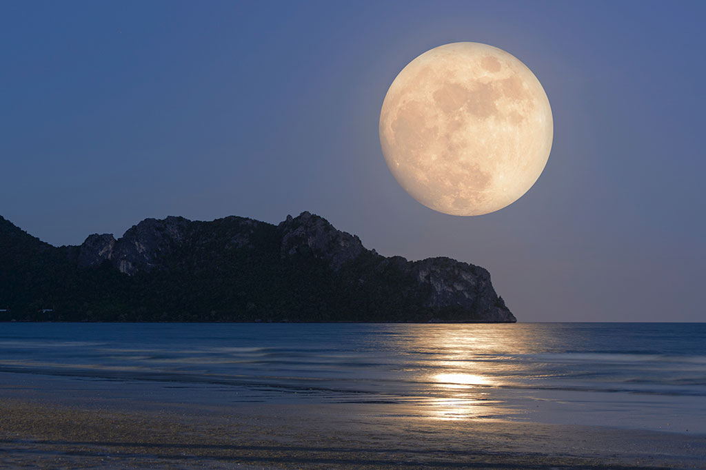 Foto da lua cheia brilhante sobre a paisagem marítima à noite.