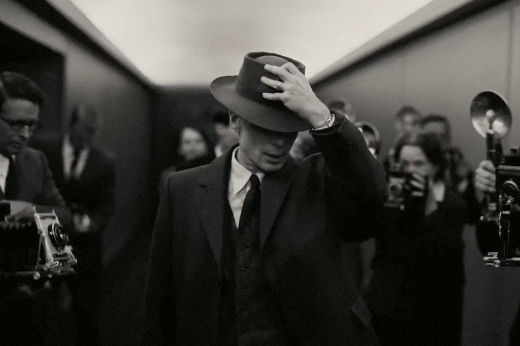 Cena do filme Oppenheimer em que Robert está cercado de fotógrafos.