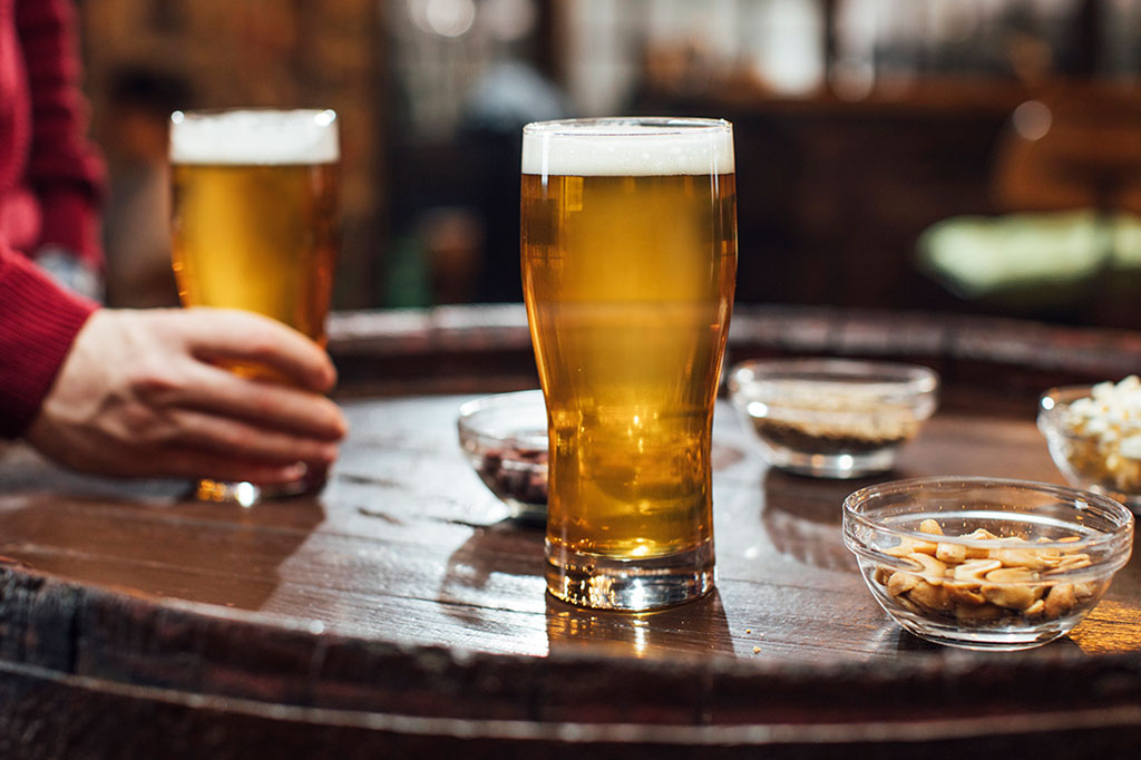 Copos de cerveja e amendoim sob uma mesa de madeira em um pub.
