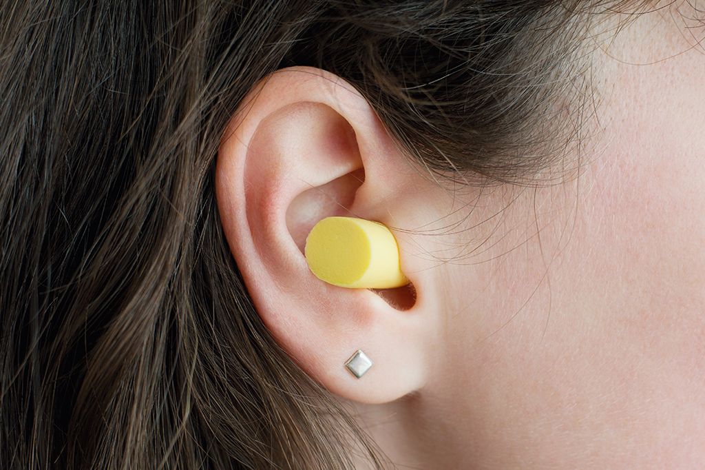 Imagem aproximada de uma mulher com um tampão de redução de ruídos na orelha.