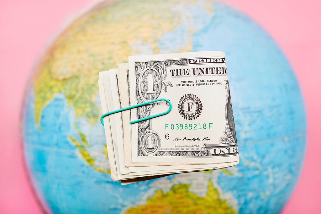 Foto de um monte de notas de dólar americano e globo em fundo rosa.