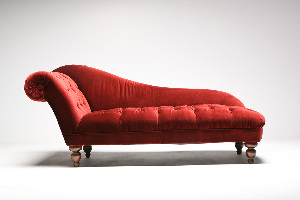 Um divã vermelho em uma sala com chão e parede brancos.