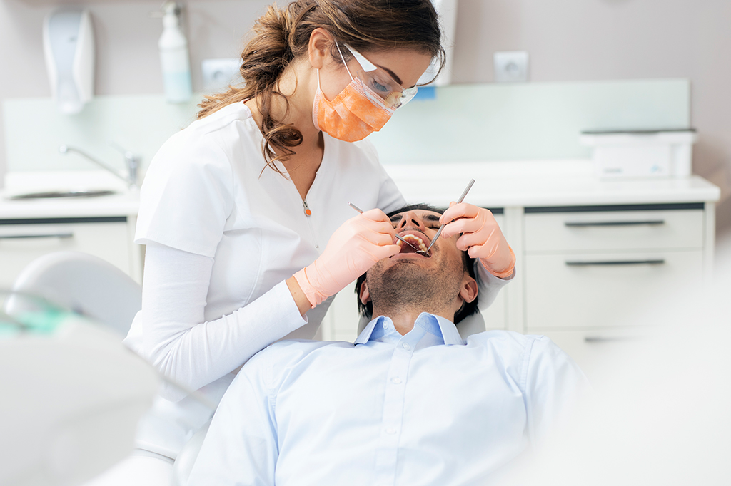 Uma dentista de EPI realizando procedimentos odontológicos em um paciente na cadeira do consultório.